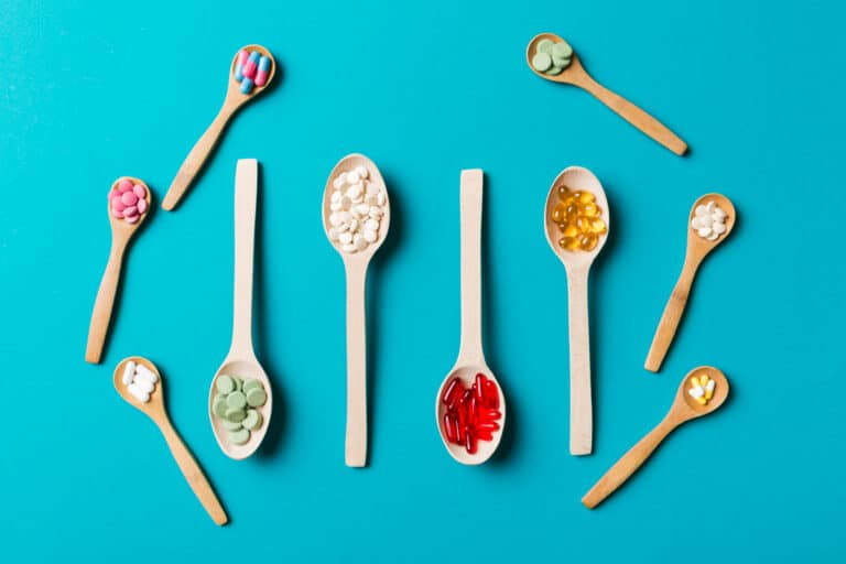 Top view Variety of vitamin and mineral pills in wooden spoon on Colored background Top view of assorted pharmaceutical medicine pills Dietary supplement healthcare product | Alliance Drawback Services Assorted vitamins and pills placed on wooden spoons arranged in a row on a teal background.